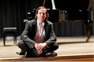 Klassischer Musiker im Frack sitzt auf Bühne vor einem Konzertflügel.