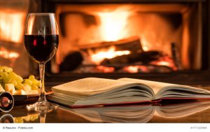 Offenes Buch mit Weinglas vor Kaminfeuer.