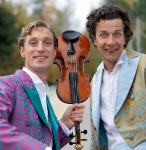 Foto zweier Musiker in einem Anzug mit einer Geiger in der Mitte.