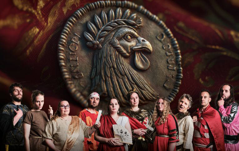 Eine Reihe von Theaterschauspieler*innen im Hintergrund eine goldene Münze mit einem Adler abgebildet