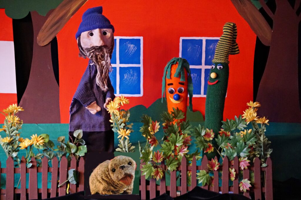 Puppen Rudi Seehund und eine männliche Puppe vor einem roten Haus