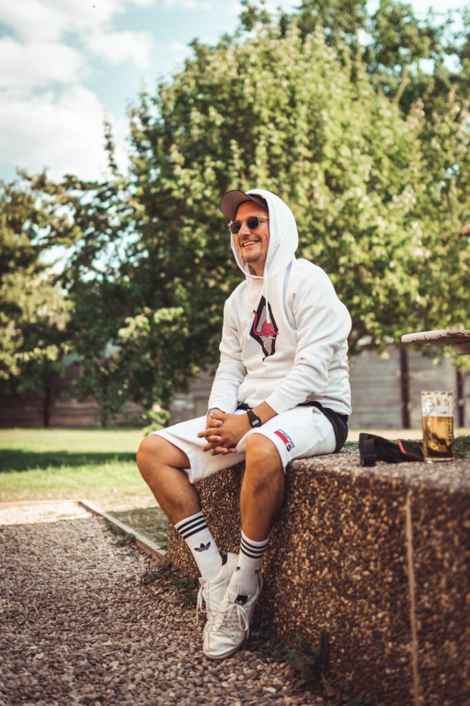 Junger Mann mit Cap und Hoodie sitz auf einer Mauer, daneben steht ein Glas Pils