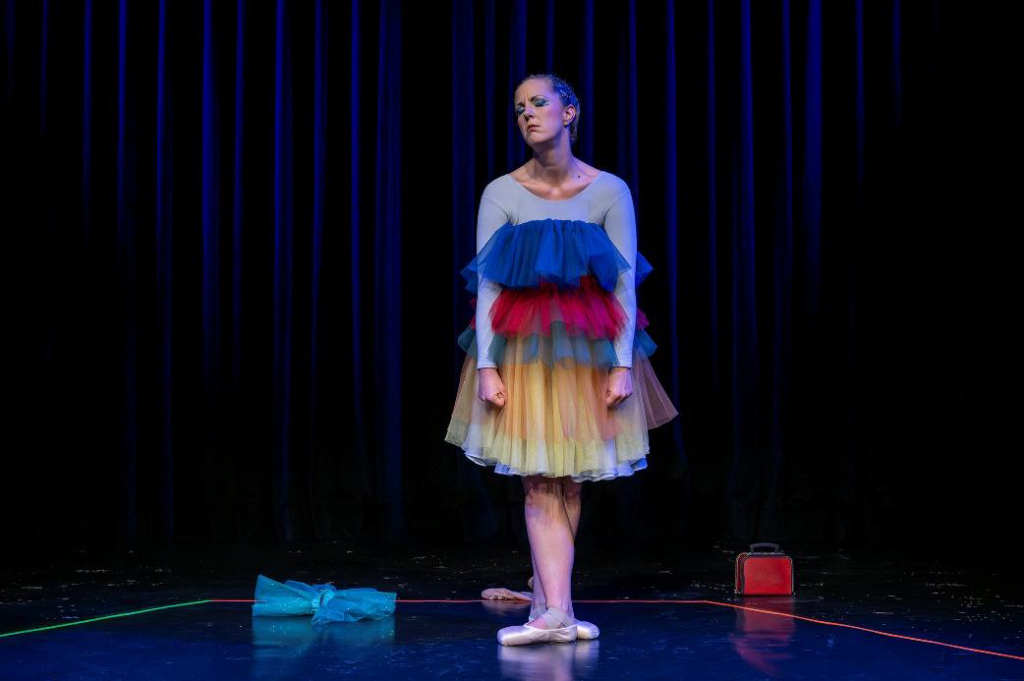 Eine Ballerina mit einem bunten Kleid mit Ballettschuhen auf der Bühne mit einem enttäuschten Gesichtsausdruck