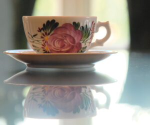 Teetasse steht auf einem Glastisch und spiegelt sich. Teetasse mit ostfriesischer Rose