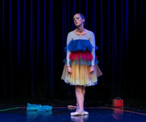 Eine Ballerina mit einem bunten Kleid mit Ballettschuhen auf der Bühne mit einem enttäuschten Gesichtsausdruck